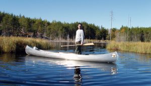 Man standing in canoe on river. A\J AlternativesJournal.ca