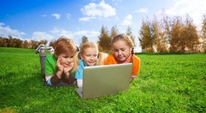 Kids using a laptop outside in a field. Alternatives Journal.