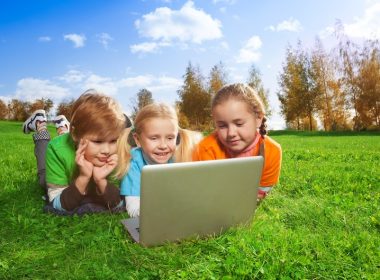 Kids using a laptop outside in a field. Alternatives Journal.
