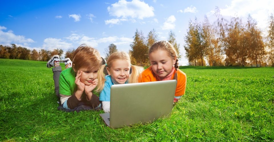 Kids using a laptop outside in a field. Alternatives Journal.