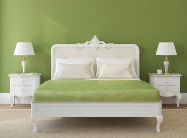 A bed with a green bedspread in front of a green wall.