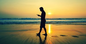 6 Super Summer Apps - man walking on a beach looking at his phone