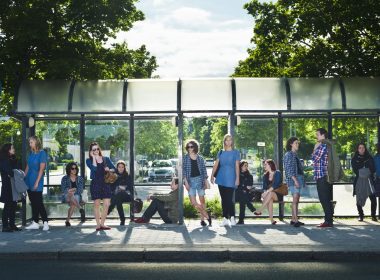 (Photo: a group of people waiting at a bus stop)