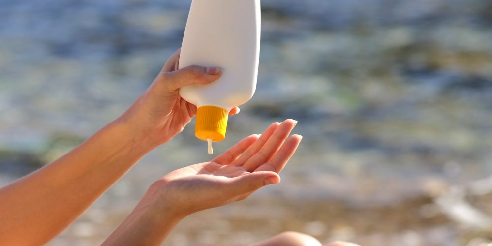 Woman putting sunscreen from a bottle on the beach