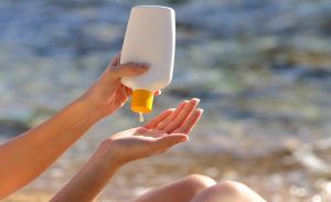 Woman putting sunscreen from a bottle on the beach