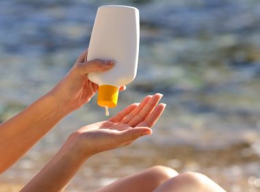 Woman putting sunscreen from a bottle on the beach