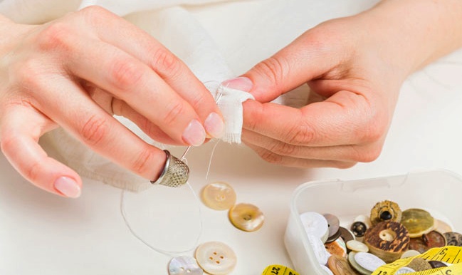 (Photo: a woman sews a button on fabric)