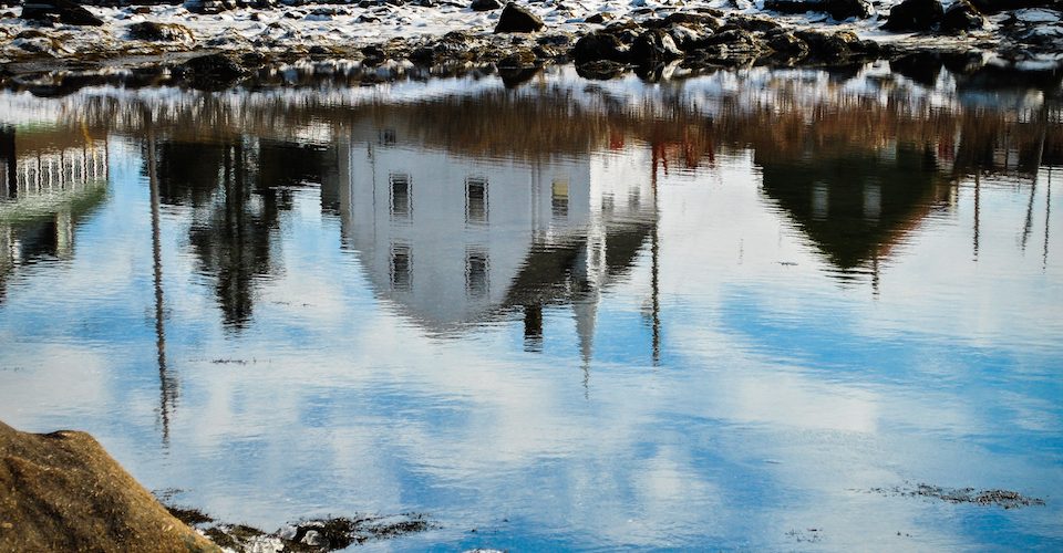 (Photo: a reflection of a village in a body of water)