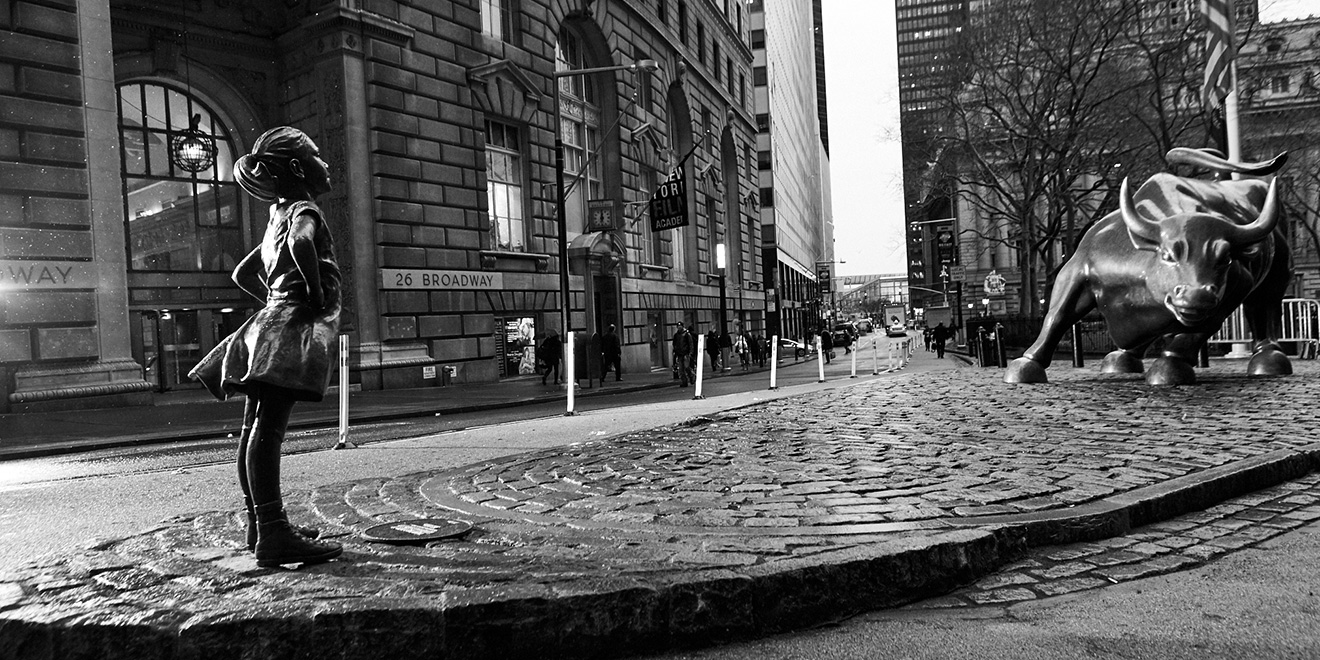 Fearless girl statue standing opposite charging bull statue